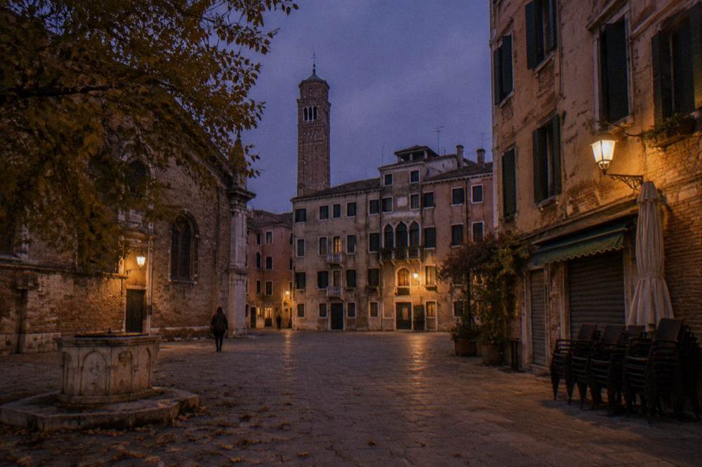An empty Venice square at dusk with shuttered windows and a distant bell tower