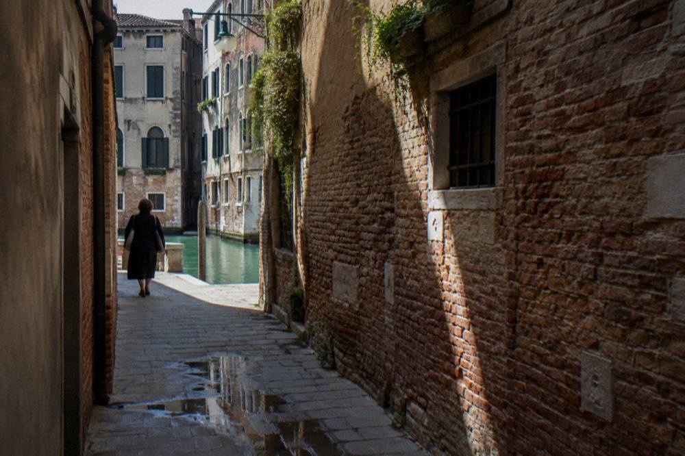 Empty Venetian alley with stone walls and a canal glimpsed between buildings