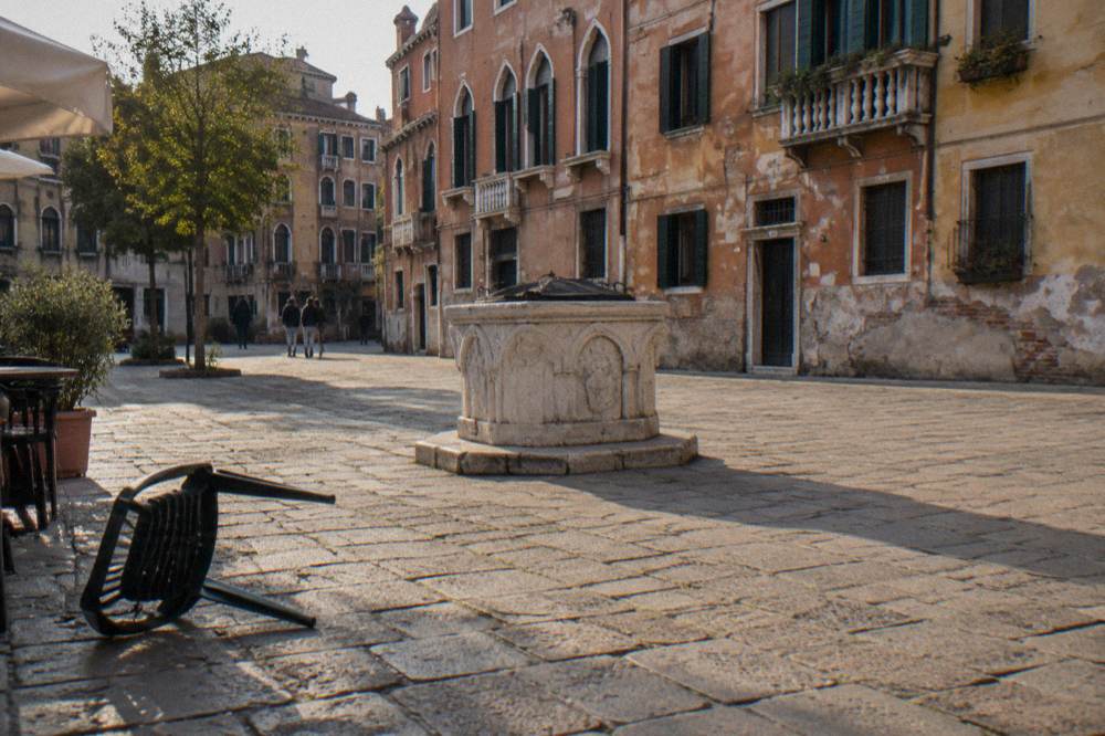 Sunlit Venice square with a well head in the centre and faded palace walls