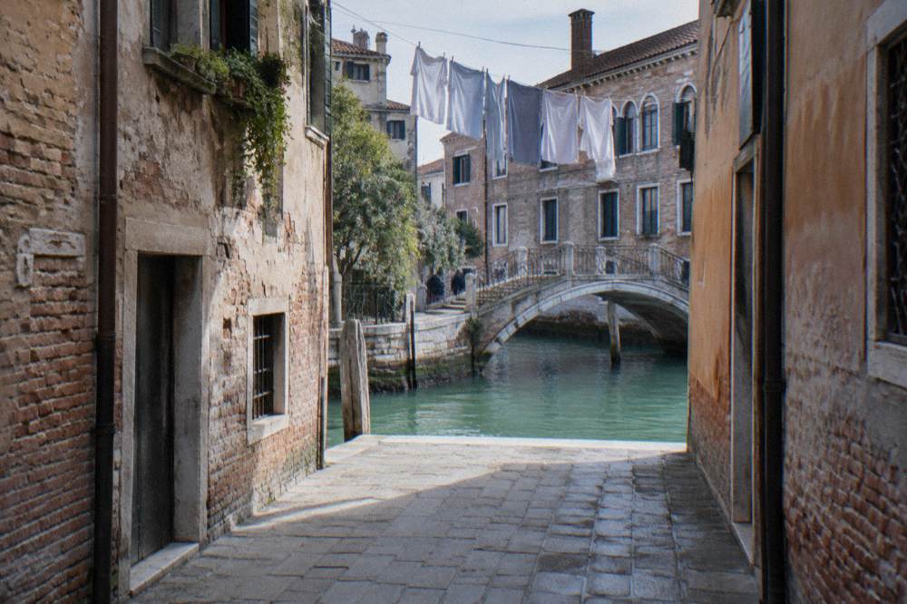 Narrow Venice street in Cannaregio opening onto a sunlit canal with a small bridge