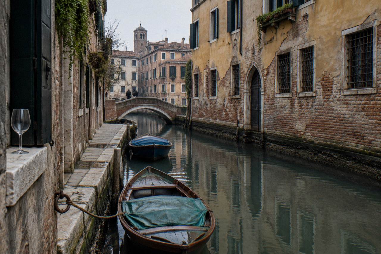 A quiet canal in a Venice backstreet with moored boats and faded palace walls