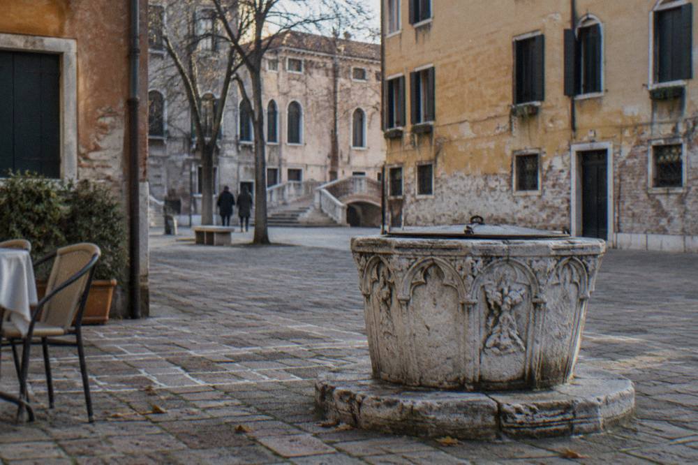 Sunlit Venetian square with a stone well head and faded plaster walls