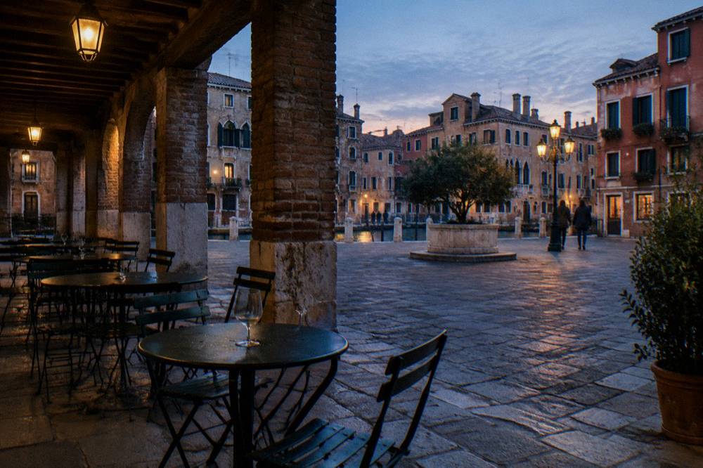 Venetian campo with cafe tables under arcades at dusk