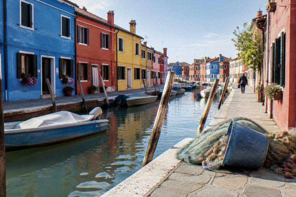 Brightly painted houses in blue, red and yellow beside a canal with moored boats