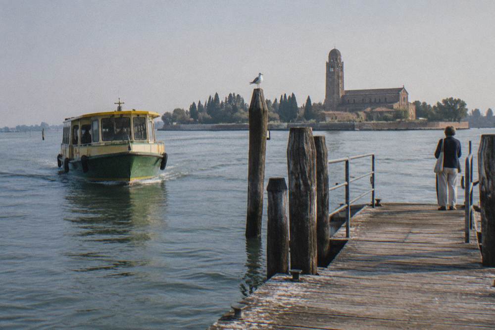 A vaporetto water bus approaching a wooden landing stage on a lagoon island