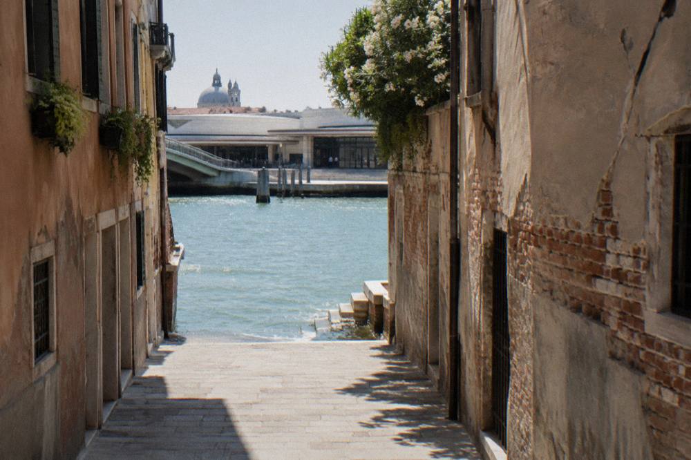 Narrow Venetian street with worn stone paving leading toward a sunlit canal
