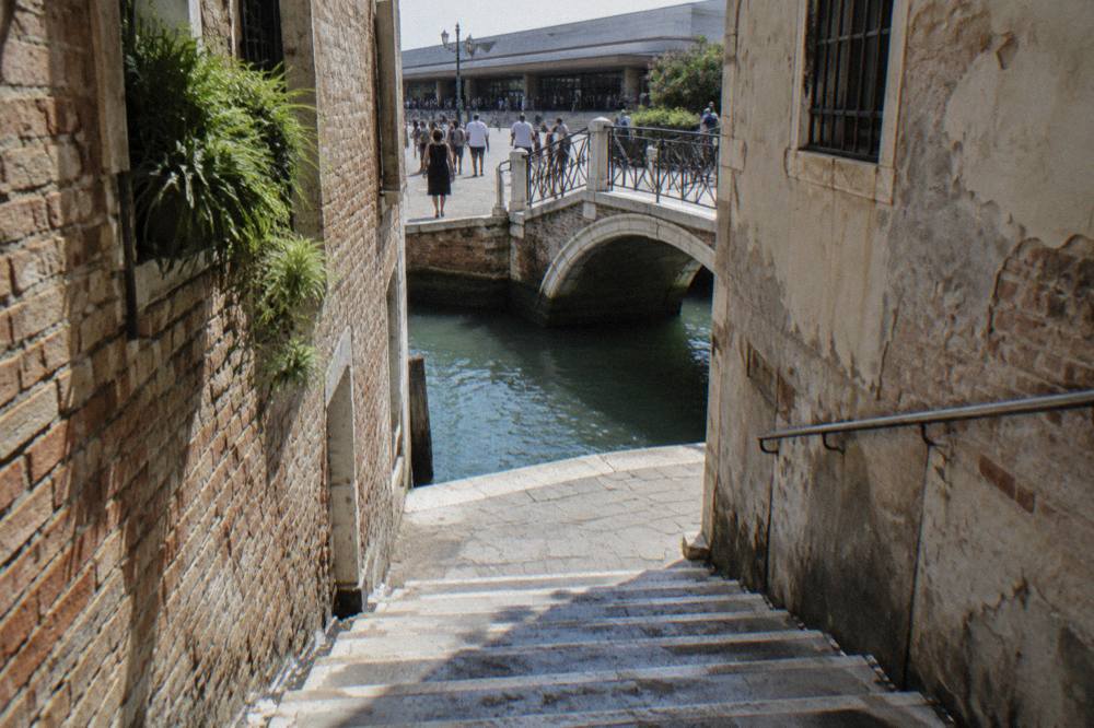 Narrow Venetian calle with brick walls, worn stone steps and a small canal crossing