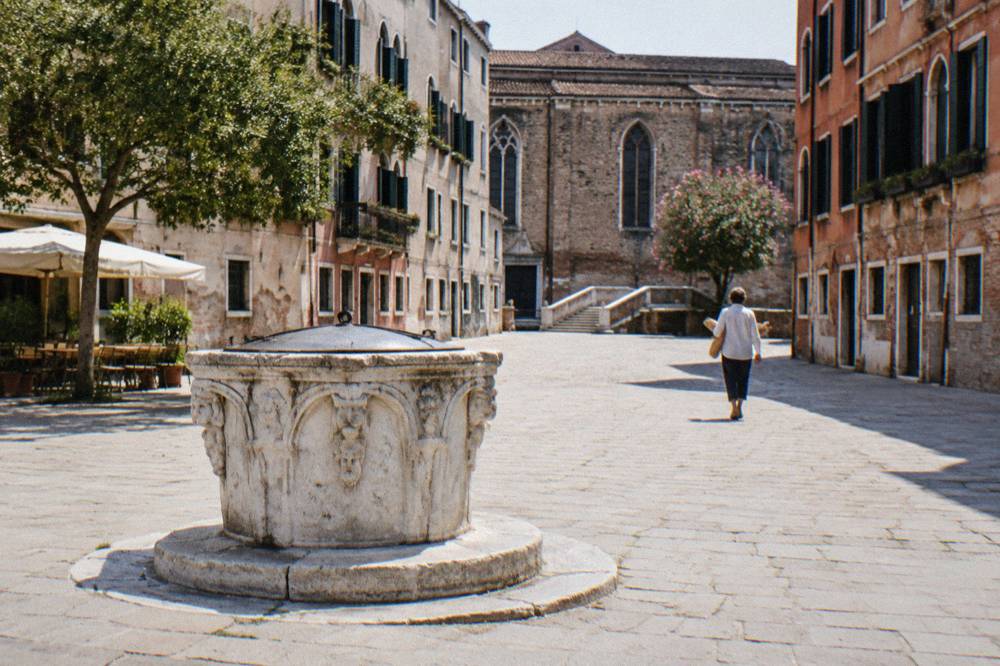Sunlit Venetian campo with an old stone well head and plain plaster facades