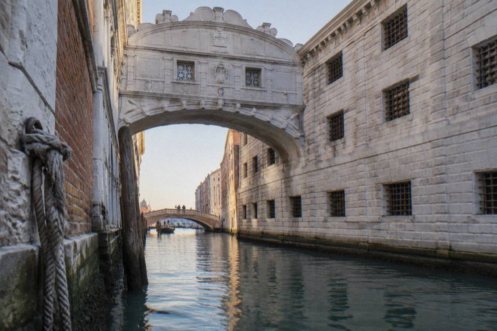 Stone bridge with small barred windows arching over a narrow canal in Venice