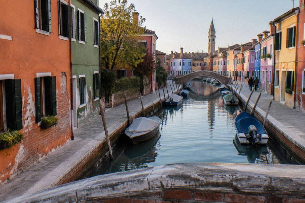 Brightly painted Burano houses in orange and green seen across a small canal
