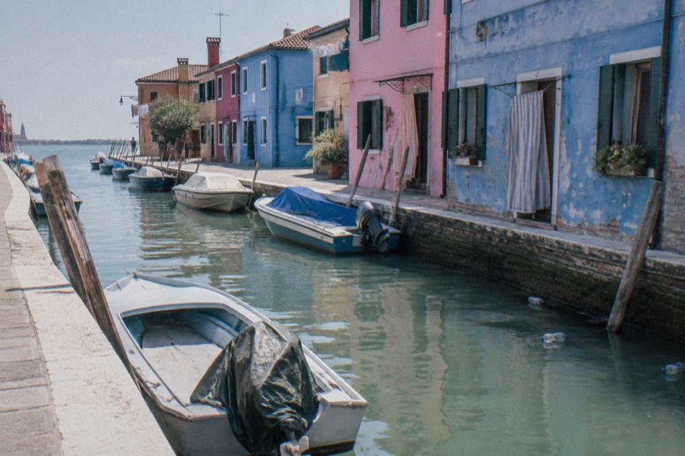 A Burano canal at midday with painted facades and moored small boats