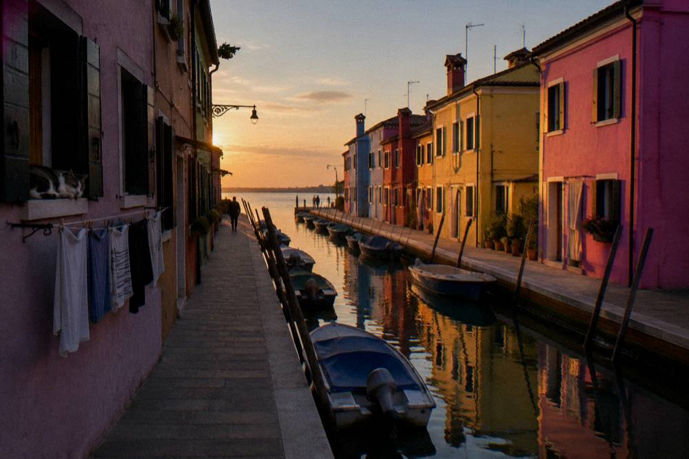 Sunlight falling on Burano houses painted in pink and yellow along a narrow canal