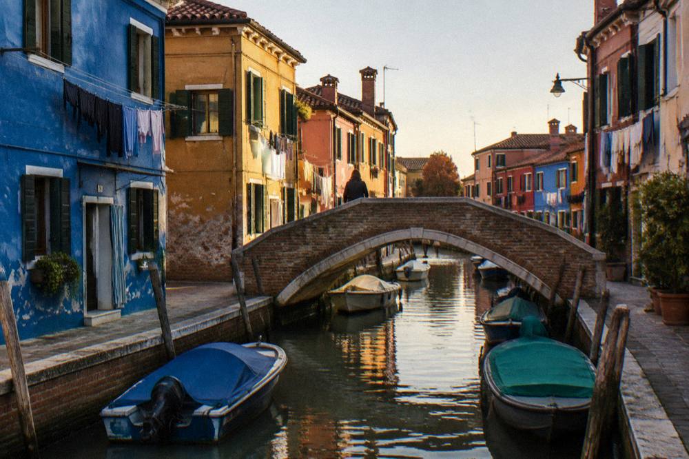 A small bridge over a Burano canal with houses in blue and ochre on both sides