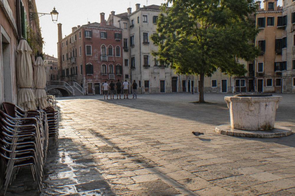 A guided walking group paused in a small Venice campo surrounded by tall facades