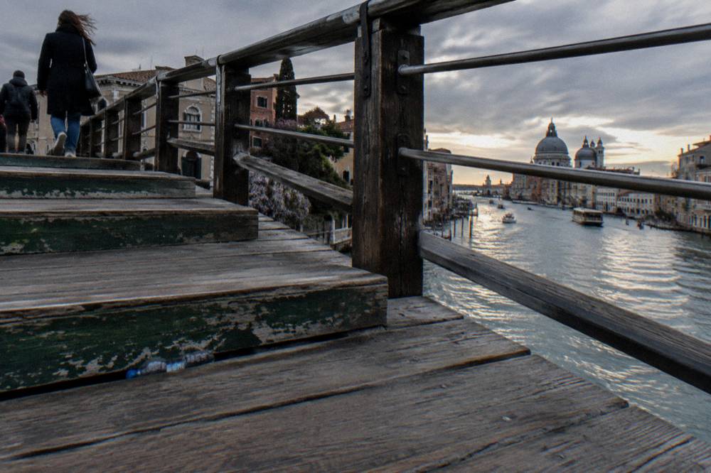A Venice canal side walk with worn brick walls and a small arched bridge