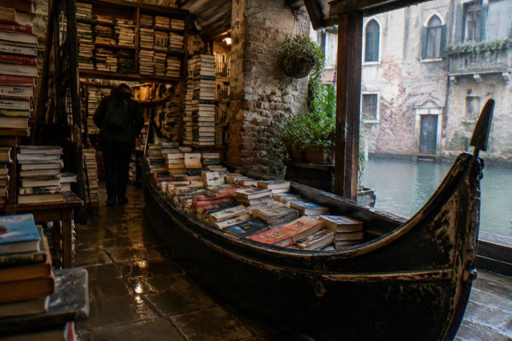 A gondola filled with books moored inside a small Venetian bookshop