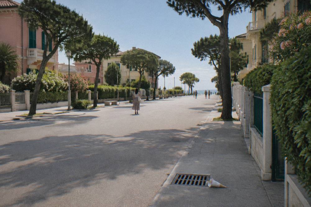 A wide flat island road lined with low trees and pastel buildings, with open water visible in the distance