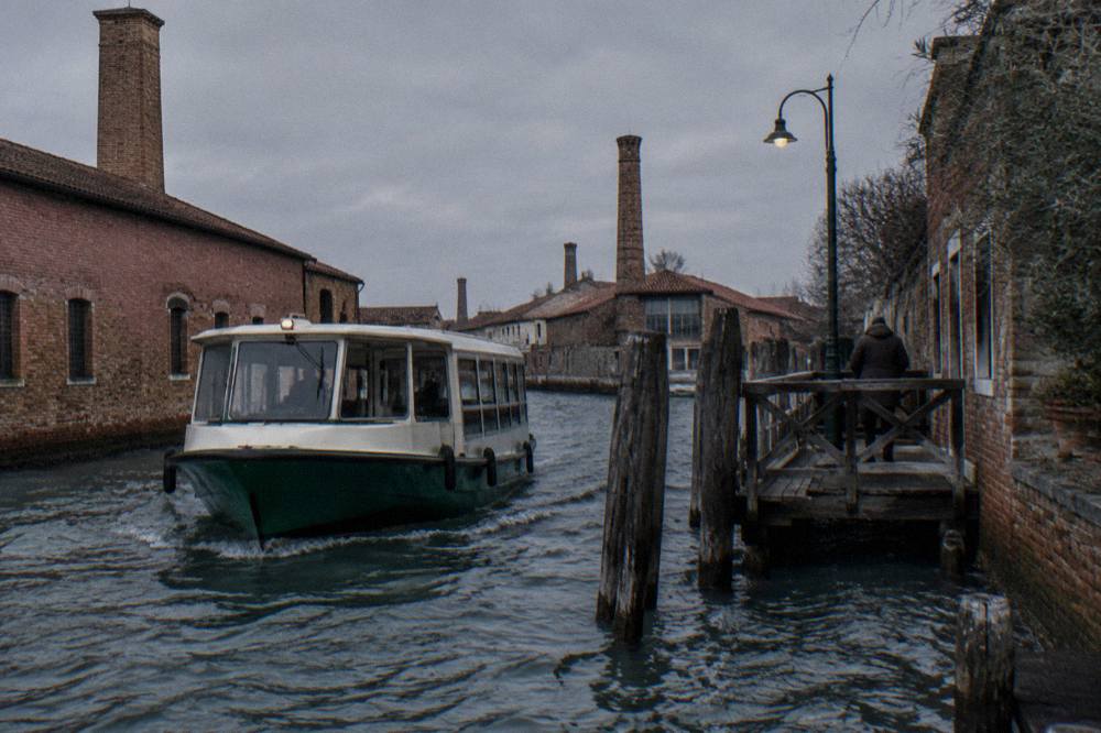 A vaporetto waterbus approaching a wooden landing stage on a lagoon channel