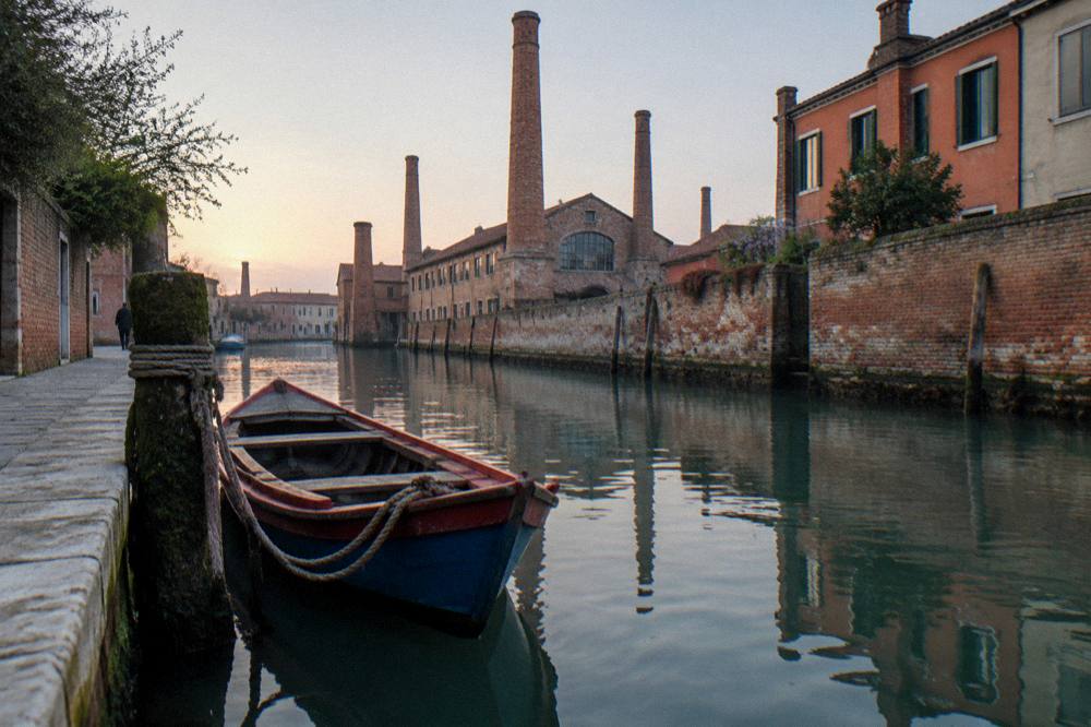 A small boat moored on a lagoon channel between islands with low buildings on both shores