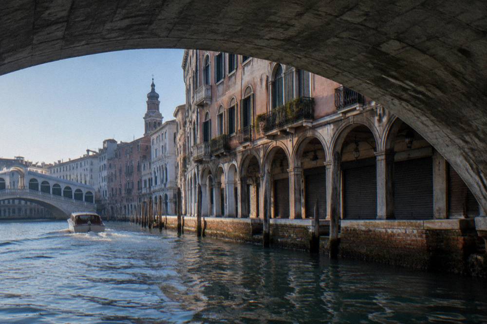 A stone bridge over the Grand Canal with arcaded shops and boats passing underneath