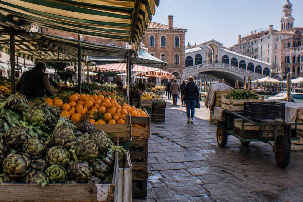 Produce stalls and awnings in the Rialto market streets with the bridge beyond the rooftops