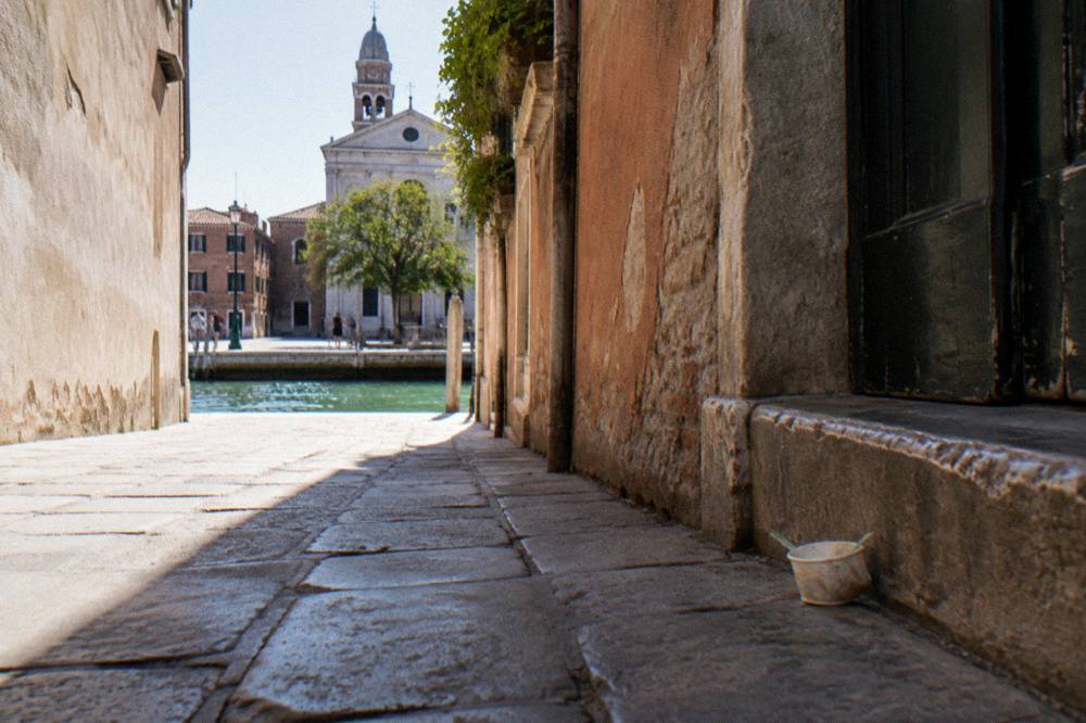 A narrow Venetian street with worn stone paving leading toward a sunlit canal