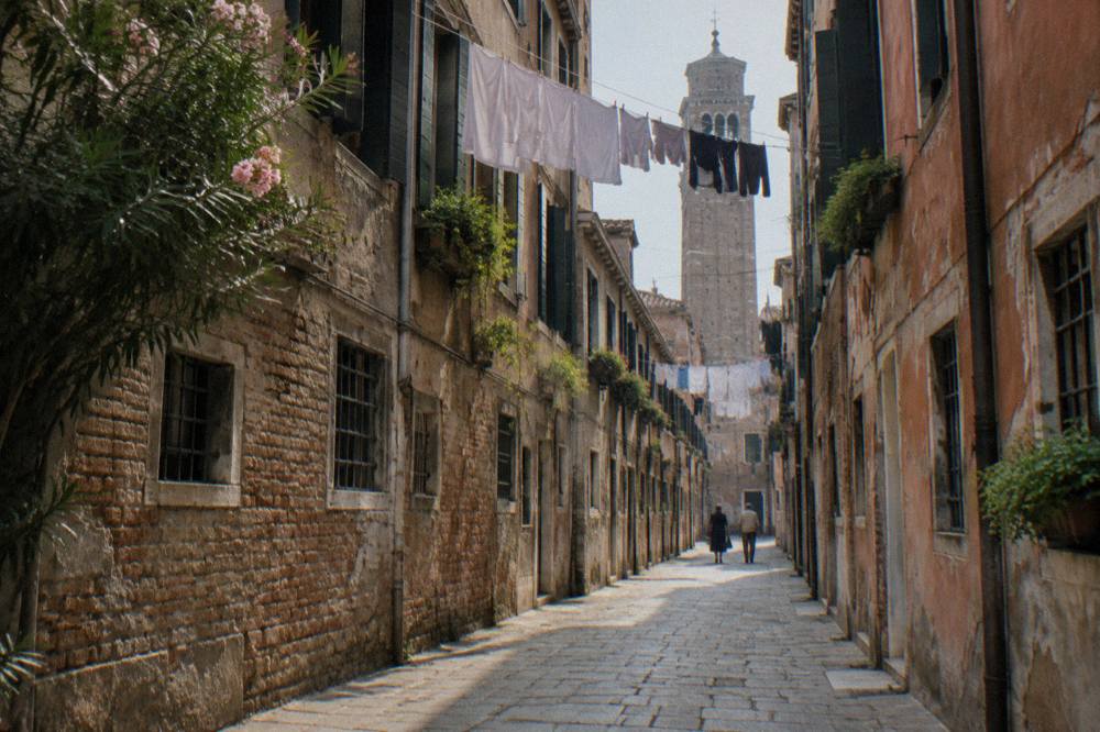 A narrow Venice street with laundry overhead and worn stone paving leading toward a distant campanile
