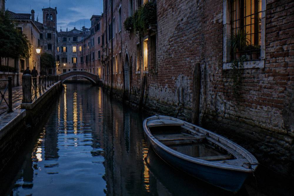 A quiet Cannaregio canal at dusk with softly lit windows reflecting on still water