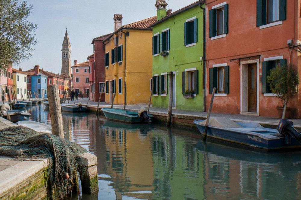 Brightly painted houses along a Burano canal with small boats tied at the waterline