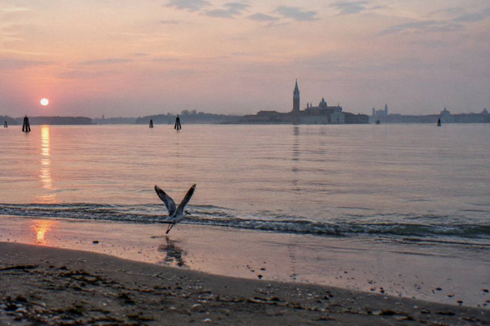 The Venice lagoon at sunrise with distant island silhouettes across calm open water