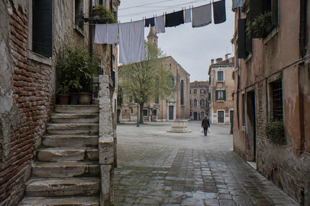 A narrow Venice calle with laundry overhead leading toward a sunlit campo