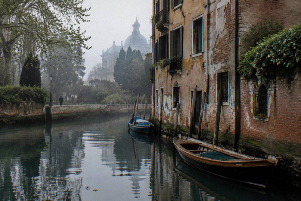 A quiet Venice canal in late afternoon light with moored wooden boats