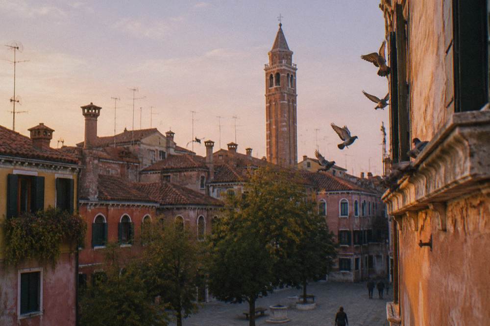 View across a Venice rooftop skyline toward a bell tower in soft light