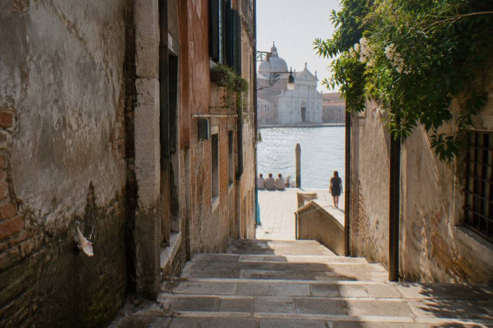 A narrow Venice alley with worn stone paving leading toward a sunlit canal