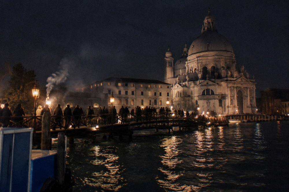 A temporary votive bridge crossing a Venice canal crowded with people walking